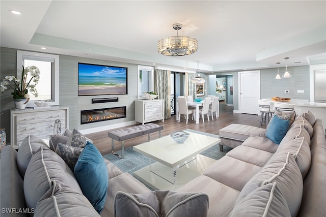 living room with an inviting chandelier, dark hardwood / wood-style floors, and a raised ceiling