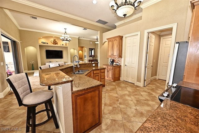 kitchen with an inviting chandelier, dark stone counters, a kitchen bar, crown molding, and sink