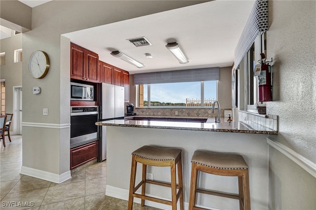 kitchen with light tile patterned floors, a breakfast bar, dark stone countertops, stainless steel appliances, and kitchen peninsula