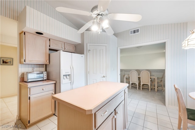 kitchen with light tile patterned flooring, light brown cabinetry, ceiling fan, white refrigerator with ice dispenser, and a kitchen island