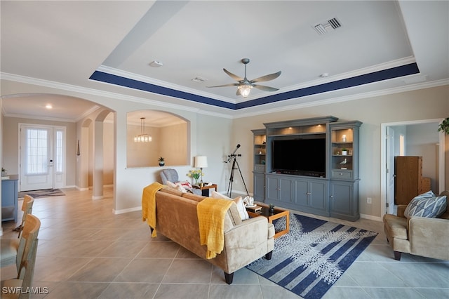 tiled living room with a tray ceiling, ceiling fan with notable chandelier, and crown molding