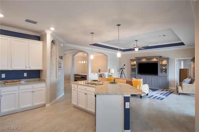 kitchen featuring decorative light fixtures, light stone countertops, an island with sink, white cabinets, and a tray ceiling