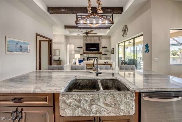 kitchen with a tiled fireplace, stainless steel dishwasher, light stone countertops, and plenty of natural light