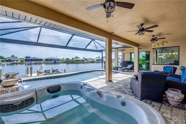 view of swimming pool with a hot tub, a water view, a patio area, glass enclosure, and ceiling fan