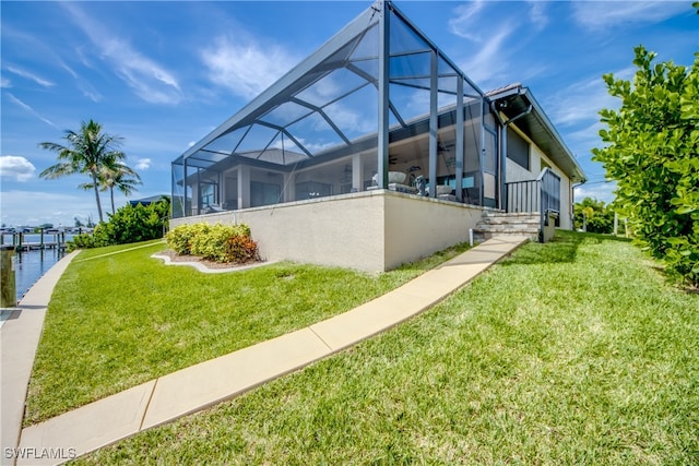 back of property with a water view, glass enclosure, and a lawn