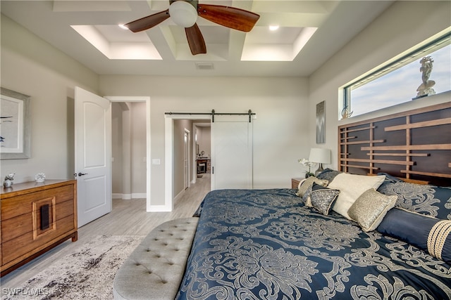 bedroom featuring a barn door, a tray ceiling, light wood-type flooring, and ceiling fan