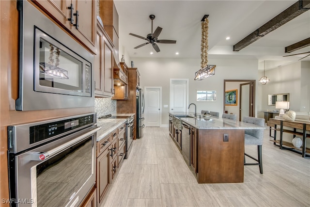 kitchen with beam ceiling, a breakfast bar, a kitchen island with sink, stainless steel appliances, and decorative light fixtures