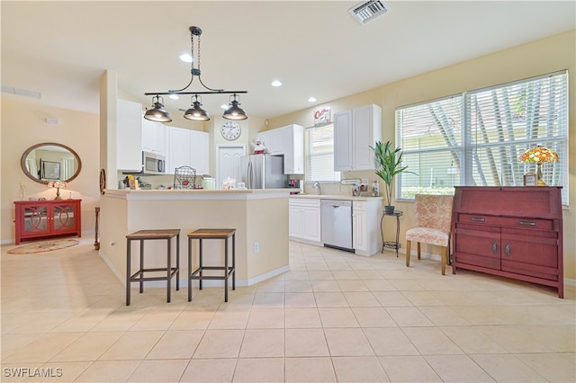 kitchen featuring a kitchen bar, stainless steel appliances, light tile patterned floors, white cabinets, and hanging light fixtures