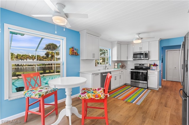 kitchen with white cabinets, decorative backsplash, appliances with stainless steel finishes, and light hardwood / wood-style flooring