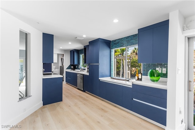 kitchen with dishwasher, blue cabinets, sink, light hardwood / wood-style flooring, and decorative backsplash