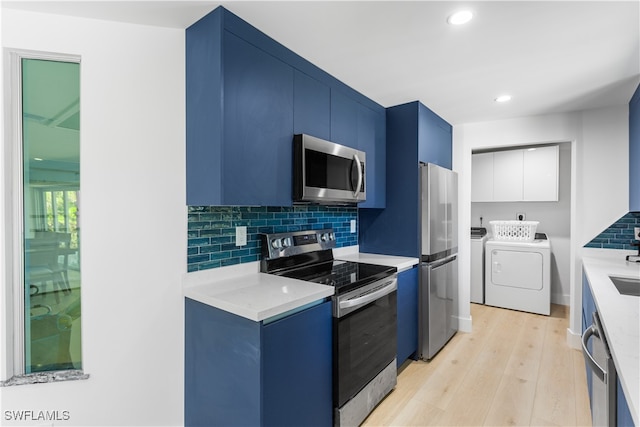 kitchen with stainless steel appliances, washing machine and dryer, blue cabinets, light hardwood / wood-style floors, and decorative backsplash