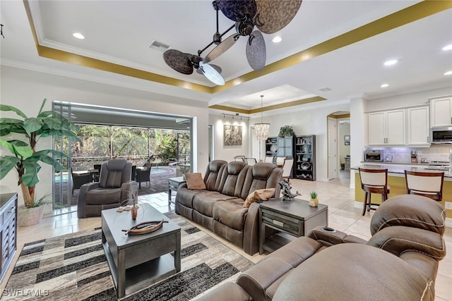 tiled living room with ornamental molding, ceiling fan, and a tray ceiling