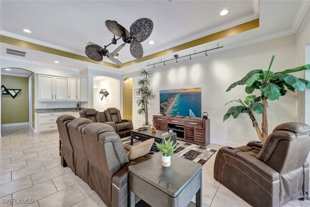 tiled living room with ceiling fan, a tray ceiling, and ornamental molding