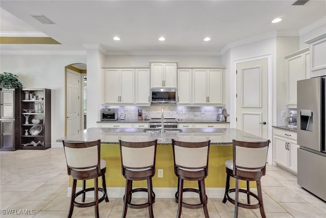 kitchen featuring light stone counters, appliances with stainless steel finishes, an island with sink, and white cabinets