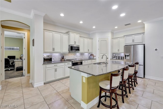 kitchen with a center island with sink, appliances with stainless steel finishes, stone countertops, sink, and a breakfast bar