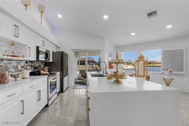 kitchen featuring tasteful backsplash, sink, white cabinetry, stainless steel appliances, and a center island with sink