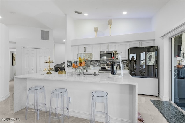 kitchen featuring white cabinetry, tasteful backsplash, appliances with stainless steel finishes, and a kitchen bar