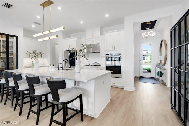 kitchen featuring white cabinets, a large island with sink, stainless steel appliances, and hanging light fixtures