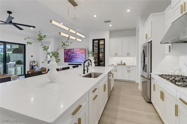 kitchen with exhaust hood, a large island with sink, sink, appliances with stainless steel finishes, and decorative light fixtures