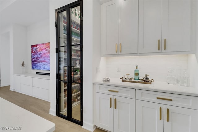 bar with decorative backsplash, light hardwood / wood-style flooring, white cabinetry, and light stone counters