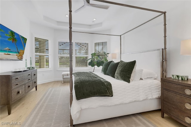 bedroom with light hardwood / wood-style flooring, a raised ceiling, and ceiling fan