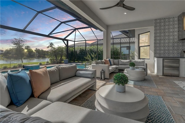 patio terrace at dusk with glass enclosure, ceiling fan, a water view, and an outdoor hangout area