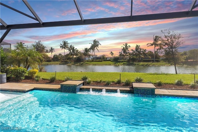 pool at dusk with pool water feature, a water view, glass enclosure, and a lawn