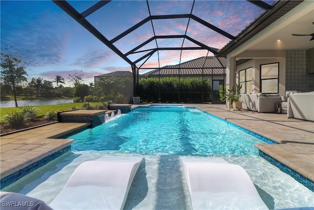 pool at dusk featuring glass enclosure, pool water feature, a water view, and a patio