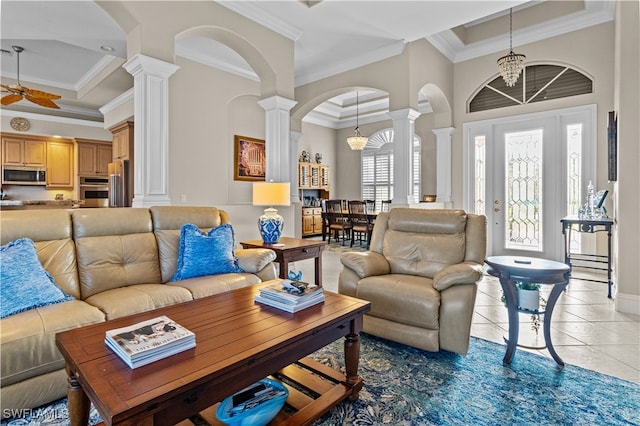 living room with tile patterned floors, ornate columns, ceiling fan with notable chandelier, crown molding, and a high ceiling