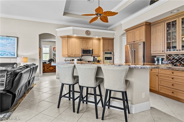 kitchen with ceiling fan, crown molding, appliances with stainless steel finishes, and an island with sink