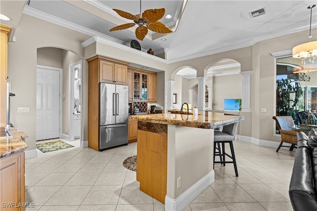 kitchen featuring light stone countertops, high quality fridge, ornamental molding, ceiling fan with notable chandelier, and a breakfast bar area