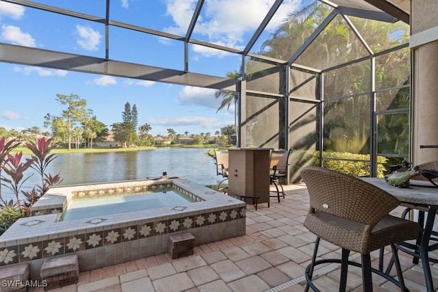 view of patio featuring glass enclosure, a water view, and an in ground hot tub