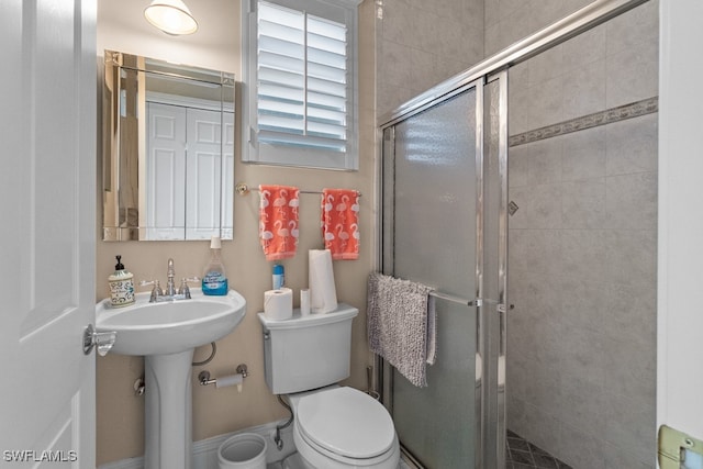 bathroom featuring toilet, a shower with shower door, and sink