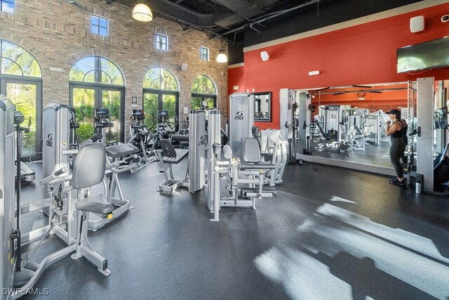 exercise room with plenty of natural light, brick wall, and a high ceiling