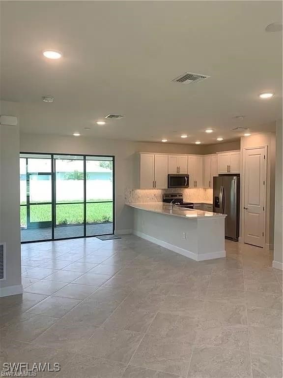 kitchen with backsplash, kitchen peninsula, stainless steel appliances, white cabinets, and light tile patterned floors