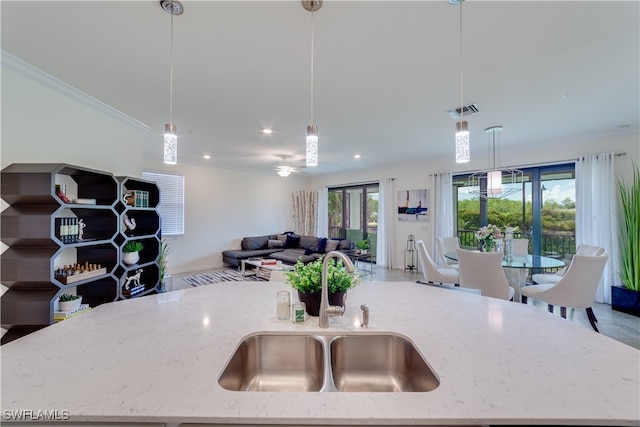 kitchen featuring a healthy amount of sunlight, sink, hanging light fixtures, and light stone counters