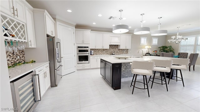 kitchen with stainless steel appliances, beverage cooler, pendant lighting, white cabinets, and an island with sink