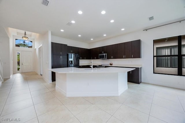 kitchen with light tile patterned flooring, dark brown cabinetry, stainless steel appliances, and an island with sink