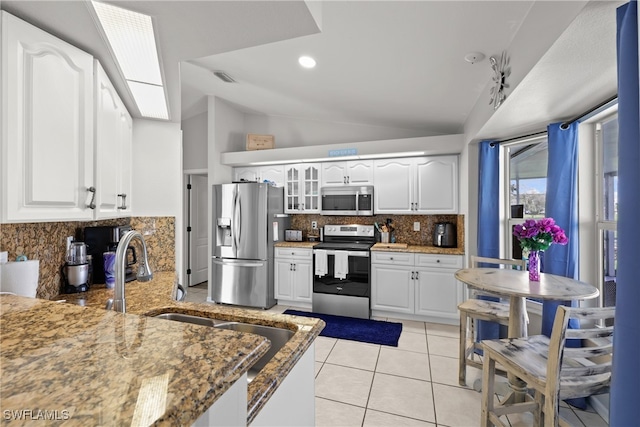 kitchen featuring white cabinetry, stainless steel appliances, vaulted ceiling, and dark stone countertops