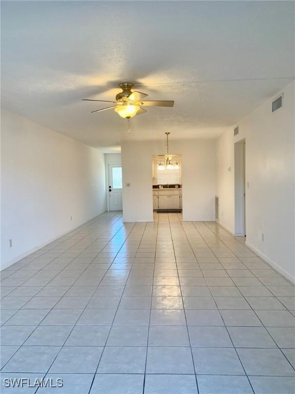 empty room featuring ceiling fan with notable chandelier and light tile patterned floors