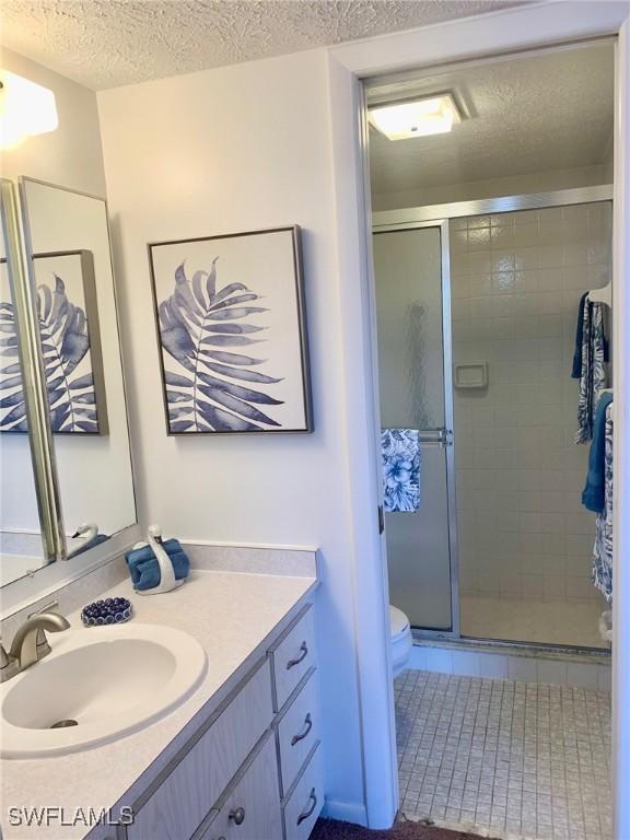 bathroom featuring walk in shower, vanity, toilet, and a textured ceiling