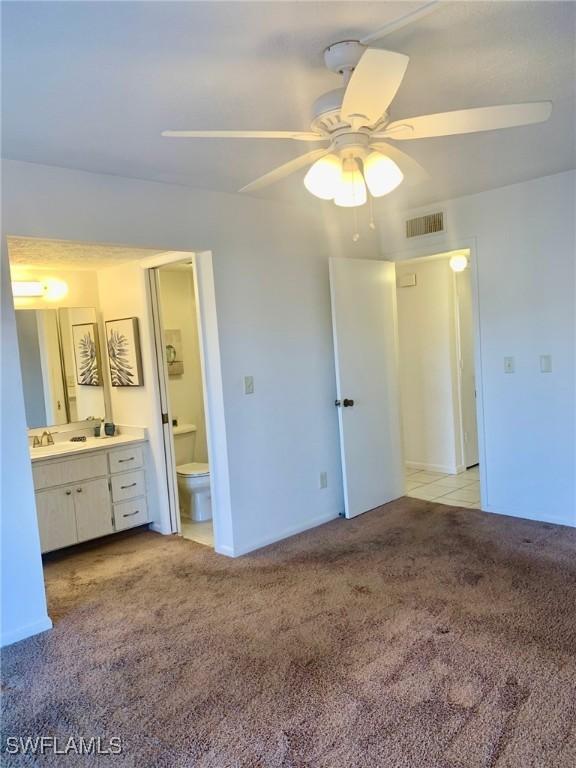 unfurnished bedroom with light carpet, sink, ceiling fan, and ensuite bathroom