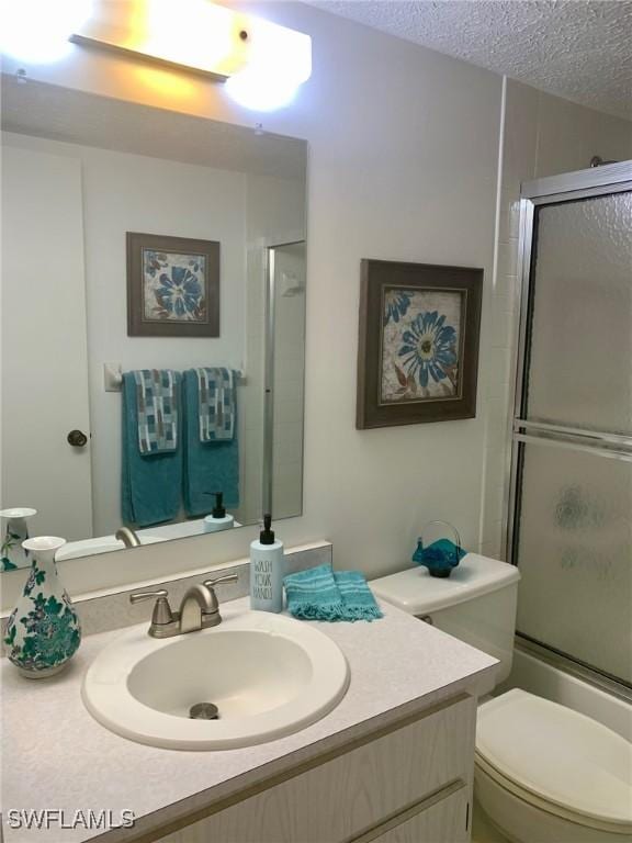 full bathroom with bath / shower combo with glass door, vanity, toilet, and a textured ceiling