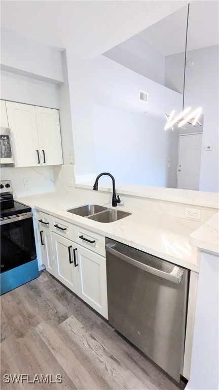 kitchen featuring light hardwood / wood-style floors, stainless steel appliances, white cabinets, sink, and decorative light fixtures