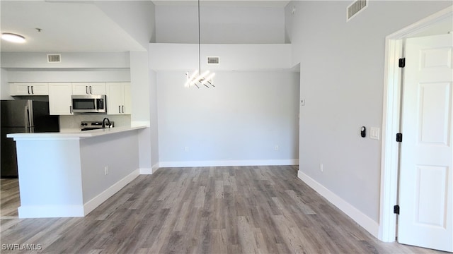 kitchen featuring kitchen peninsula, light hardwood / wood-style flooring, white cabinetry, appliances with stainless steel finishes, and decorative light fixtures