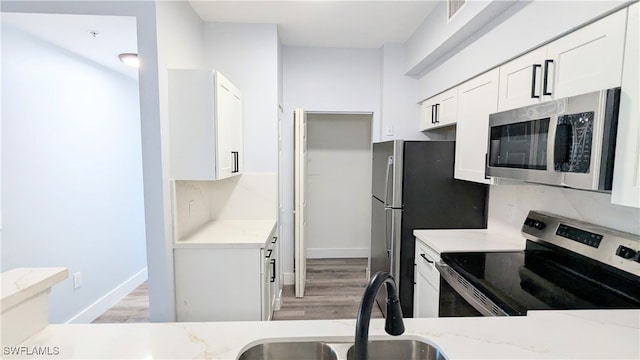 kitchen with appliances with stainless steel finishes, sink, light stone counters, and white cabinets