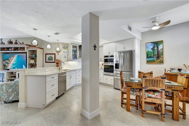 kitchen featuring kitchen peninsula, stainless steel appliances, decorative light fixtures, white cabinetry, and a textured ceiling