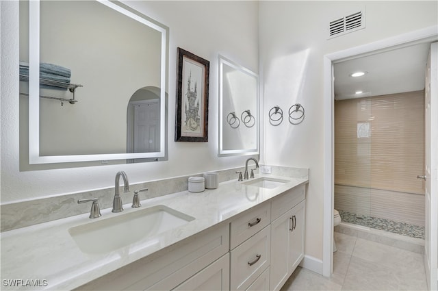 bathroom with vanity, tiled shower, toilet, and tile patterned flooring