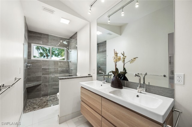 bathroom with toilet, visible vents, a tile shower, and a sink