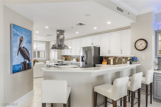 kitchen featuring a kitchen bar, stainless steel fridge, white cabinets, and island range hood